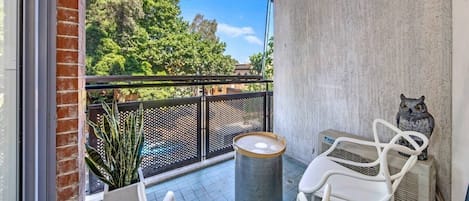 A balcony with a view of trees, a white chair, a table, and a decorative owl statue.
