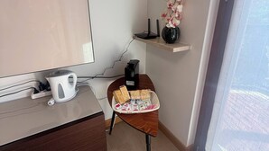 Ein modernes Hotelzimmer mit einem Holztisch, einem Wasserkocher, einer Snackkörbchen, einer kleinen Ablage mit einer Vase und einem Fenster mit Blick.