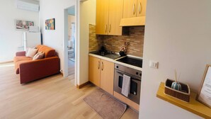 Eine kompakte Küche mit Holzausstattung, einem Edelstahl-Spülbecken und einem Backofen. Im angrenzenden Wohnbereich befindet sich ein rotes Sofa.