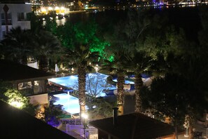 A nighttime view of a resort with a pool area, palm trees, and a distant cityscape. - CASA SOLADA CUNDA RESORT & SPA (Ayvalık)