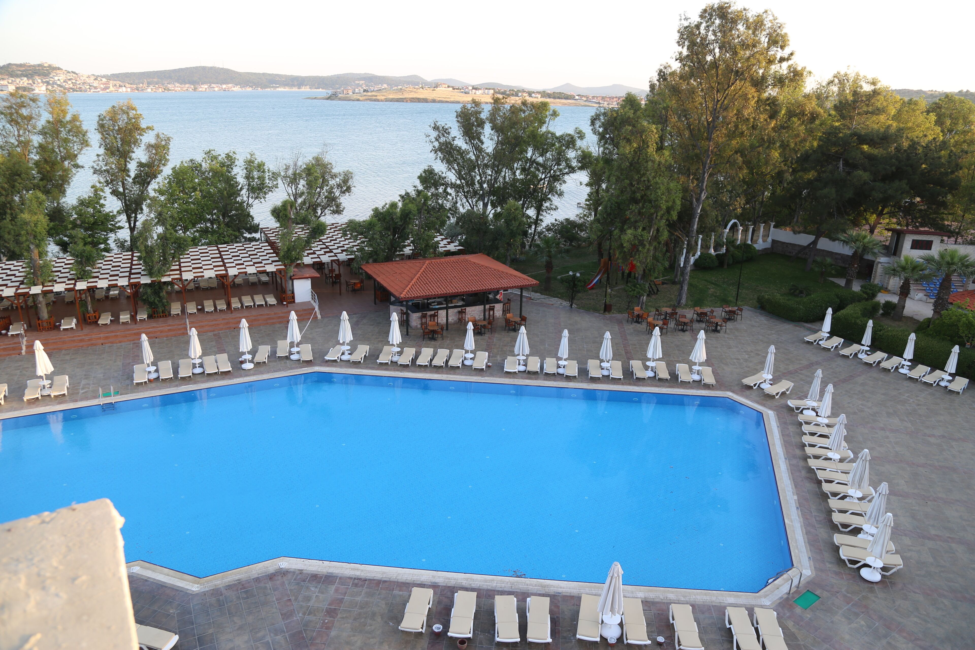 A swimming pool with lounge chairs and umbrellas, surrounded by trees and a view of the sea.