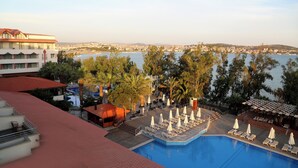 A pool area with lounge chairs and umbrellas, a building with a red roof, and a view of the sea and hills in the background. - CASA SOLADA CUNDA RESORT & SPA (Ayvalık)