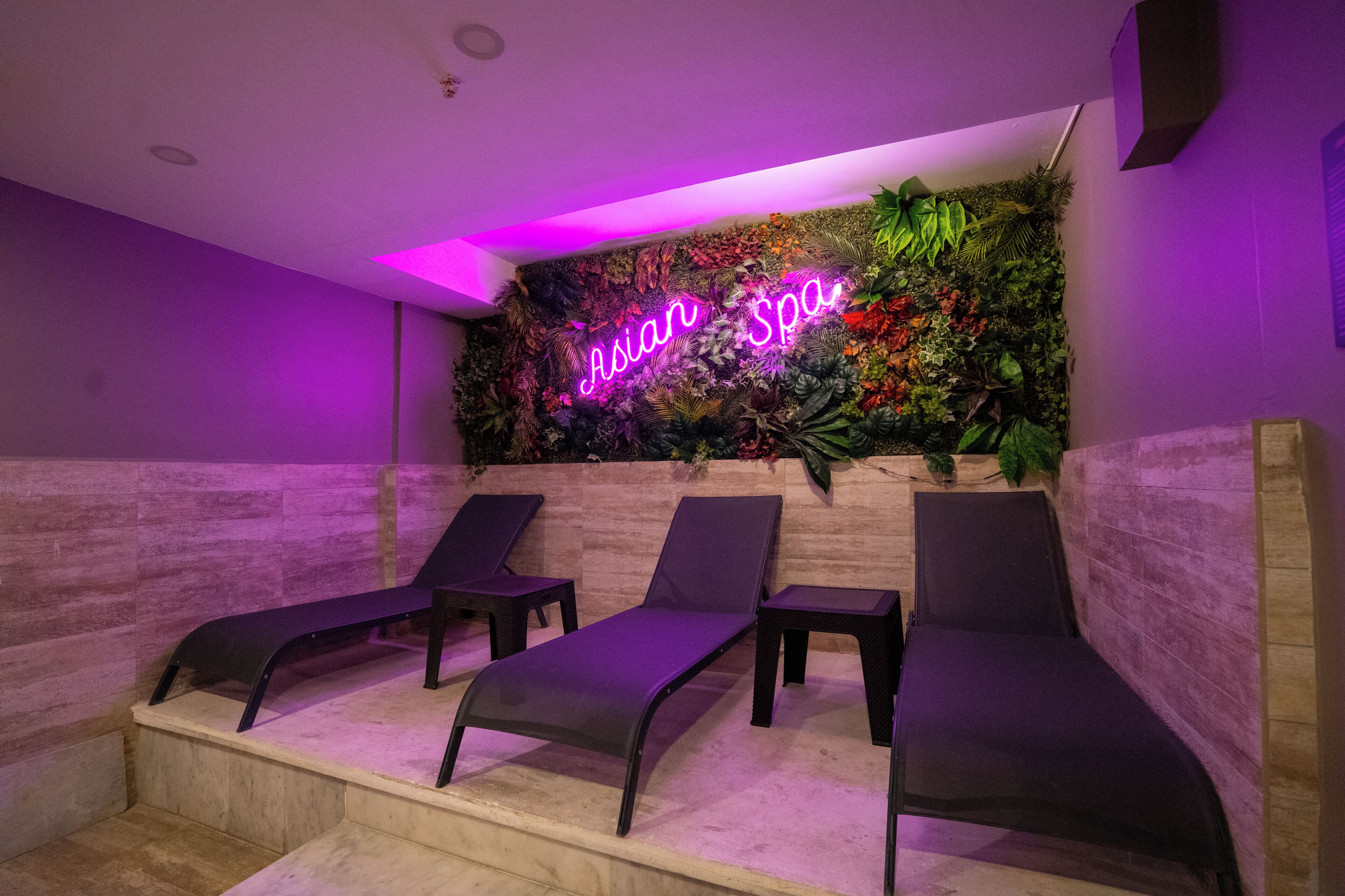 A spa area with a neon sign reading 'Asian Spa' and three lounge chairs.