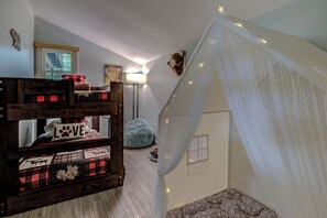 Un lit superposé pour enfant avec un coussin orné du mot « AMOUR », un fauteuil en forme de poire, une petite fenêtre et un ciel de lit blanc.