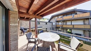 Ein Balkon mit Tisch und Stühlen, Blick auf ein mehrgeschossiges Gebäude und eine Steinmauer.