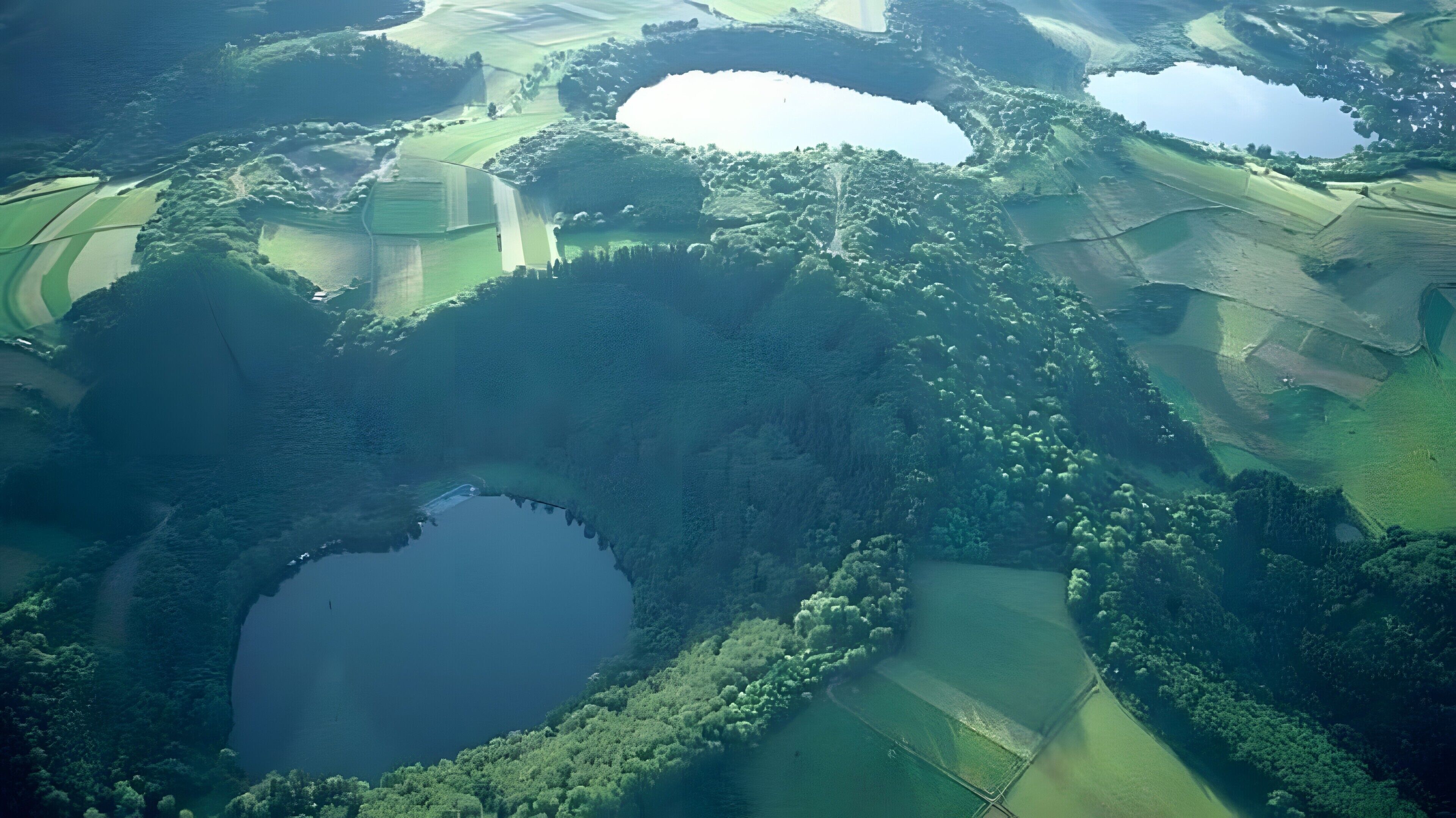 Eine Vogelperspektive auf eine Landschaft mit mehreren Teichen, umgeben von grünen Feldern und dichten Wäldern.
