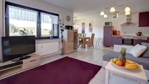 Een moderne woonkamer met een televisie, een eethoek en een keuken met een magnetron en oven.