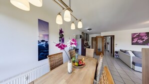 Een moderne eetruimte met een houten tafel, een fruitschaal en decoratieve bloemen.