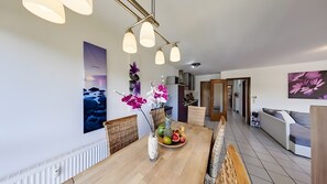 A modern dining area with a wooden table, fruit bowl, and decorative flowers.
