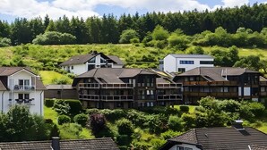 Een woonwijk met huizen in zowel traditionele als moderne stijl, omgeven door weelderige begroeiing en een bebost heuvel.