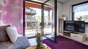 A modern living room with a sofa, a television, and a sliding glass door leading to an outdoor patio.