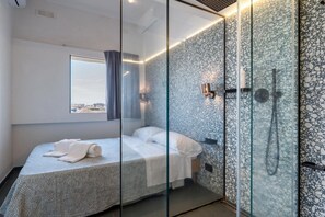 Ein modernes Hotelzimmer mit Bett, Duschkabine aus Glas und Blick auf die Stadt.