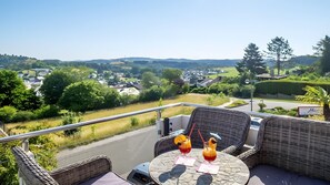 En balkon med fletningsmøbler, et bord med en drink og udsigt til et boligområde.