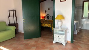 A room with a green door, a green sofa, a bed with a yellow blanket, a white bedside table with a lamp, and a bathroom with a toilet and sink. - Holiday Home in Villa I Cedri with Pool in Park, 10 Minutes from Siena (Carpineta)