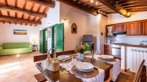 A dining area with a wooden table set for four, a green sofa, and a kitchen with wooden cabinets.