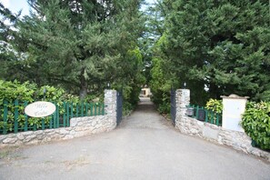 A stone-walled entrance with a green metal gate, a sign reading 'Villa Cedri,' and a gravel path leading to a building. - Holiday Home in Villa I Cedri with Pool in Park, 10 Minutes from Siena (Carpineta)