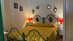 Un letto con struttura in metallo e biancheria a righe gialle, due abat-jour e specchi fissati alla parete.