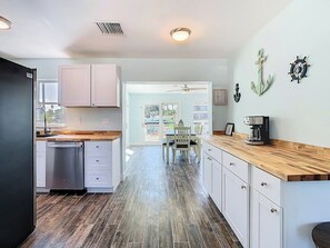 Une cuisine moderne avec des meubles blancs, un plan de travail en bois et une vue sur l’extérieur.