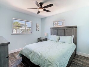 Une chambre à coucher comprenant un lit, un ventilateur de plafond, une table de chevet, une fenêtre et une commode.