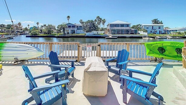 A waterfront patio with blue chairs, a covered table, and a green boat. -  Waterfront,Private Beach • Dock • Kayaks, Grill ,Firepit,SUN,HeatedPool,3 Beds (Hernando Beach)