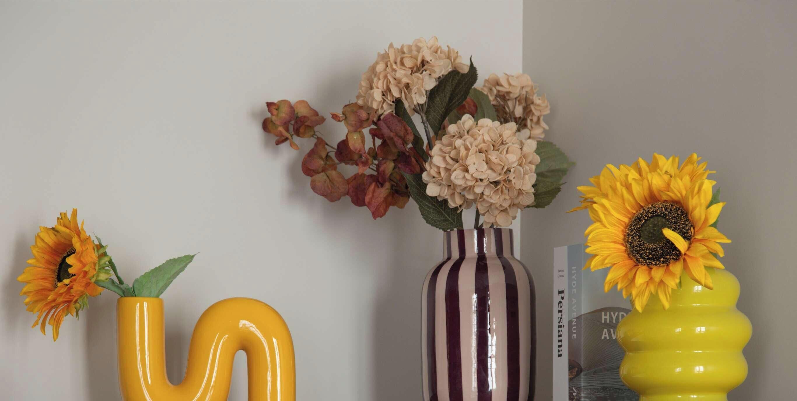 A room with a large letter 'U' on the wall, a striped vase with flowers, and a yellow vase with a sunflower.
