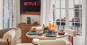 Ein Frühstückstisch mit Tellern, Früchten und einer Saftkaraffe, ein Bücherregal mit Büchern und ein Schild mit der Aufschrift 'NETFLIX'.