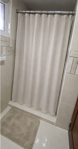 Ein Badezimmer mit Duschvorhang, einem kleinen Teppich und gefliesten Wänden.