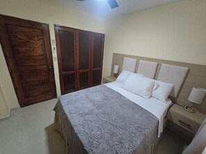 Ein Schlafzimmer mit einem Bett, Nachttischen, einem Holzschrank und einem Deckenventilator.