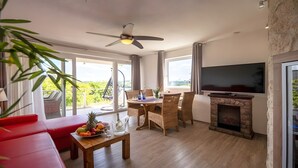 A living room with a fireplace, a TV, a dining table with chairs, and a balcony with a hanging chair.
