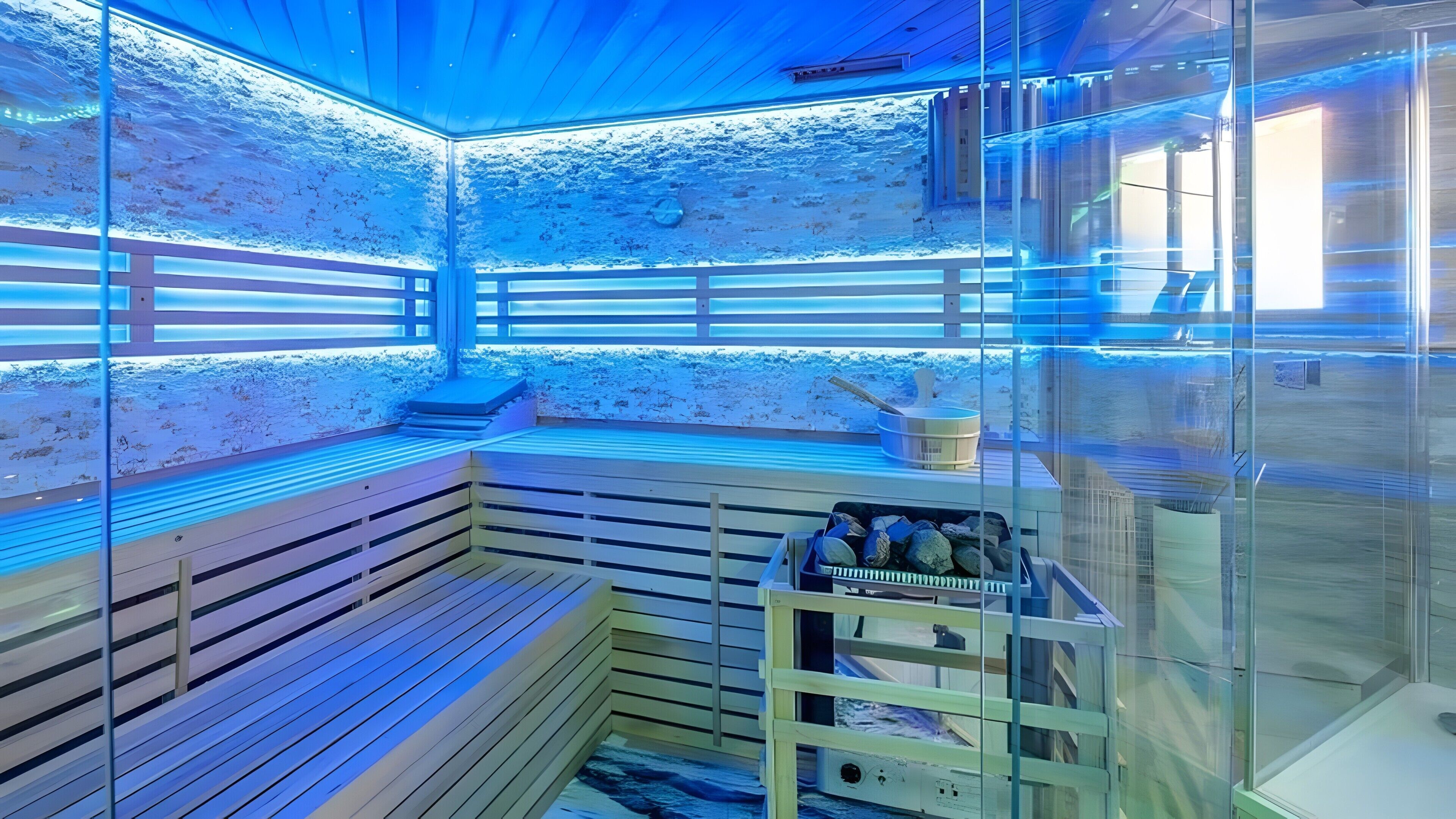 Un sauna avec des bancs en bois, des murs en verre et un plafond éclairé de lumière bleue.