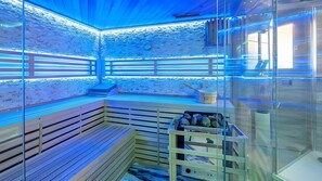 Eine Sauna mit Holzbänken, Glaswänden und einer blau beleuchteten Decke.
