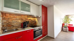 Une cuisine moderne avec des meubles de rangement rouges, un pare-feu en pierre et un four encastré.