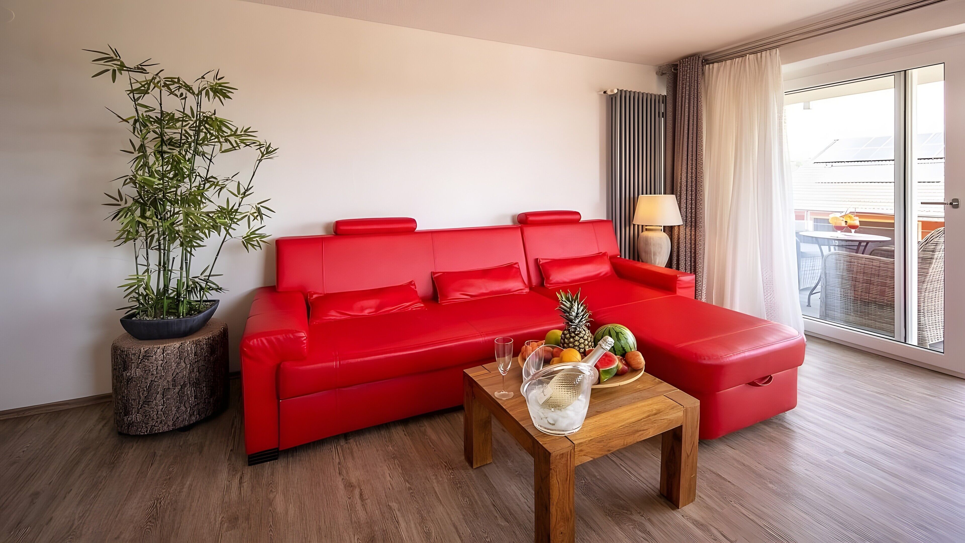 Ein rotes Sofa, ein Couchtisch mit Obst, eine Bambuspflanze und Blick ins Freie.