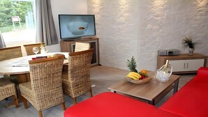 A modern living room with a television, dining table, wicker chairs, a red sofa, and a fruit bowl.