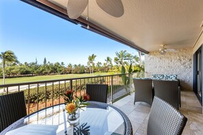 Ein Balkon mit Korbmöbeln, einem Glastisch und Blick auf einen Golfplatz.