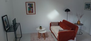 Un salon moderne avec un canapé rouge, une petite table ronde ornée d’une plante, un lampadaire noir et un tableau abstrait encadré accroché au mur.