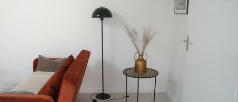 A living room with a sofa, a floor lamp, a small table with a vase, and a framed picture on the wall.