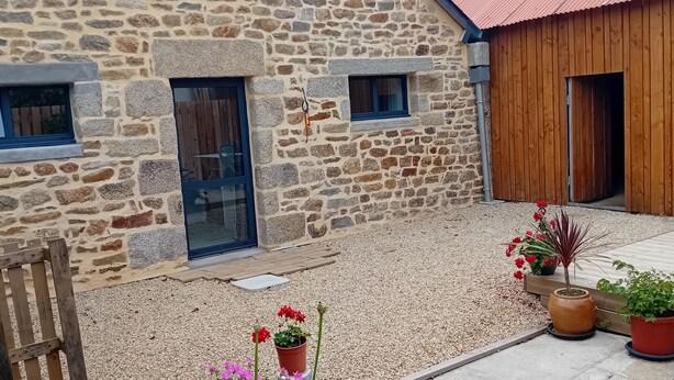 A stone building with a wooden door, a window, and a gravel patio with potted plants.