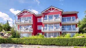 A multi-story red building with balconies, large windows, and a well-maintained garden. - Stylish Apartment for 6 People (54 m²) in Schalkenmehren (Schalkenmehren)