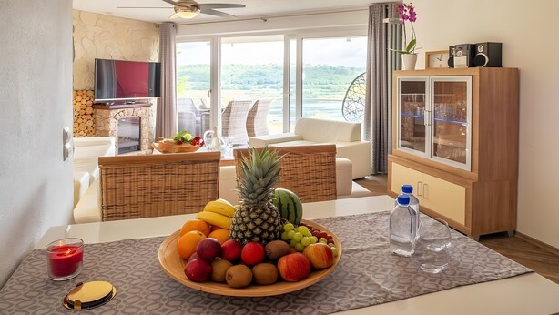 Un coin repas avec un panier de fruits, une bougie et une bouteille d’eau, le tout posé sur une table à motifs.