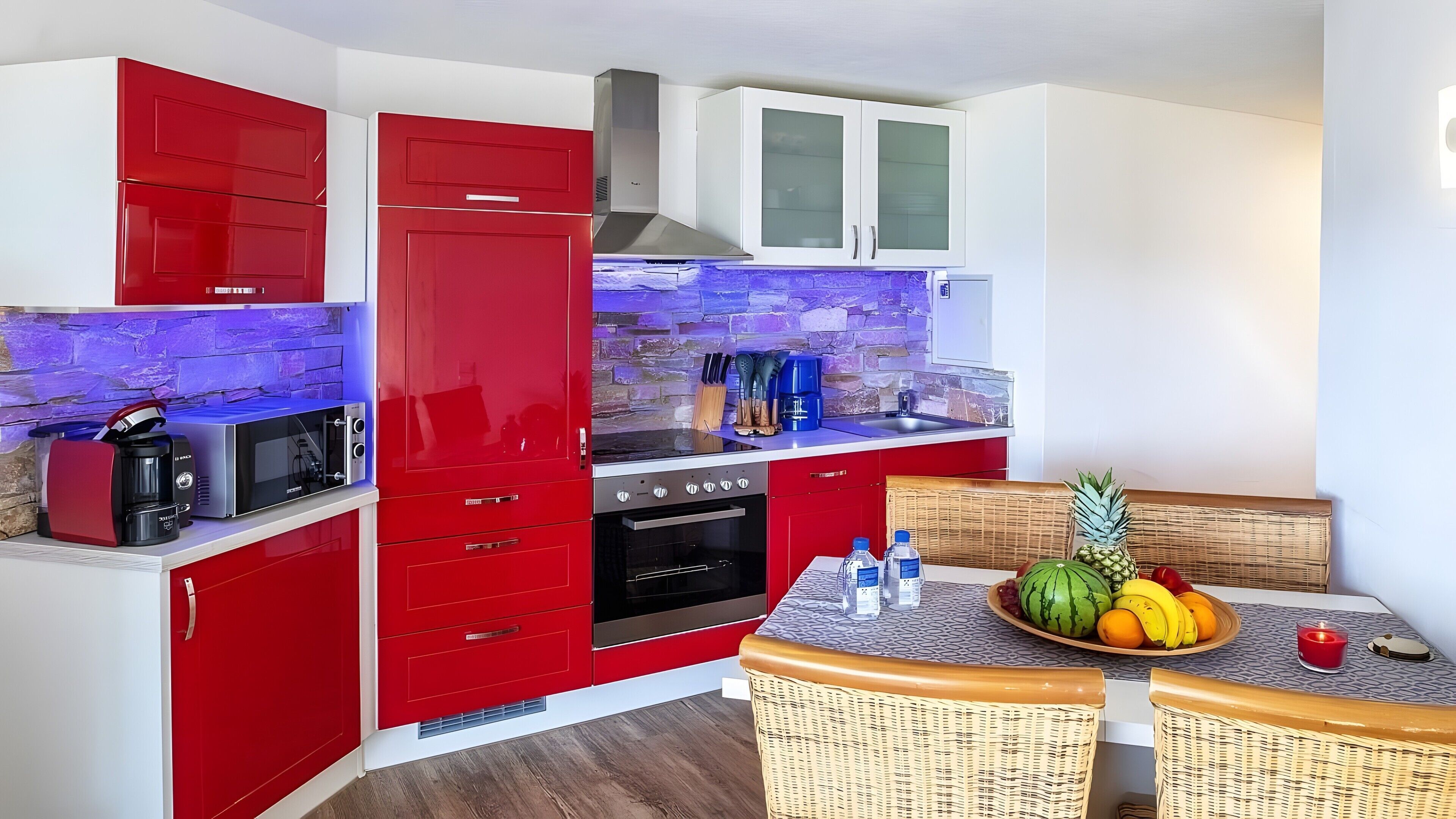 A compact kitchen with red cabinets, a microwave, a stove, and a dining area with wicker chairs.