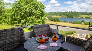 A balcony with wicker furniture, a glass table, and a view of a lake and hills. - Stylish Apartment for 6 People (54 m²) in Schalkenmehren (Schalkenmehren)