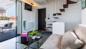 Una sala de estar moderna con un sofá, una mesa de centro con libros y una planta, un televisor montado en la pared y una escalera de diseño original.