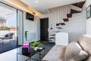 Ein modernes Wohnzimmer mit einer Couch, einem Couchtisch mit Büchern und einer Pflanze, einem an der Wand befestigten Fernseher und einer Treppe mit einem einzigartigen Design.