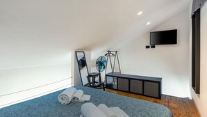 Un dormitorio moderno con cama, escritorio, ventilador y televisor.