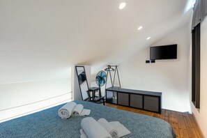 Ein modernes Schlafzimmer mit Bett, Schreibtisch, Ventilator und Fernseher.