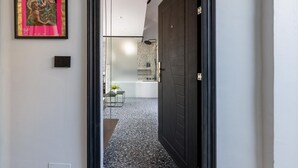 Un pasillo con un cartel enmarcado, una puerta negra y una vista parcial de un baño con ducha y lavamanos.