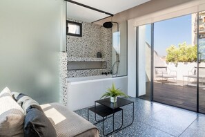 Ein modernes Badezimmer mit einer freistehenden Badewanne, einer Duschkabine aus Glas und einem kleinen Tisch mit einer Pflanze.