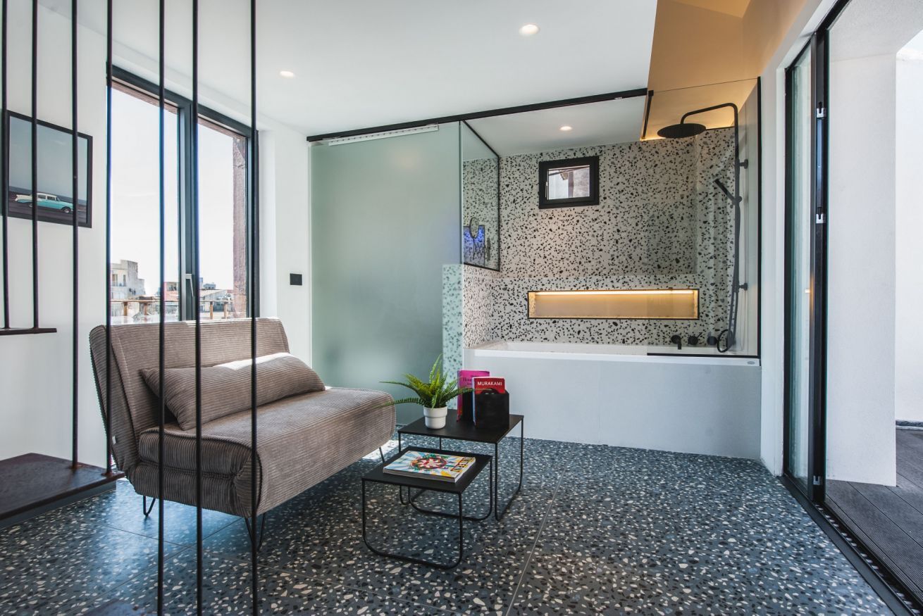A modern room with a sofa, a small table with a magazine, a plant, and a bathtub with a showerhead.