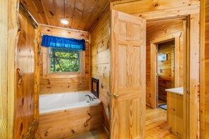 Ein Badezimmer einer Holzhütte mit Badewanne, einem Fenster mit blauen Vorhängen und einer Holztür.